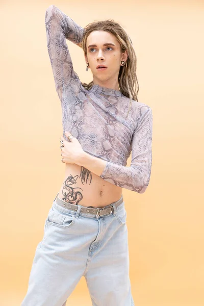 Stylish tattooed queer person posing isolated on yellow — стоковое фото