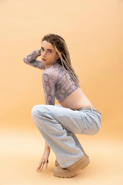 Young queer person in jeans and crop top posing on yellow background — Photo de stock