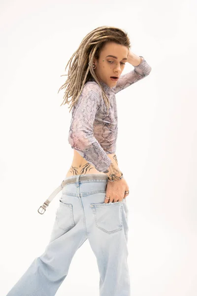 Tattooed queer person in crop top with snakeskin print and jeans posing isolated on white — стоковое фото