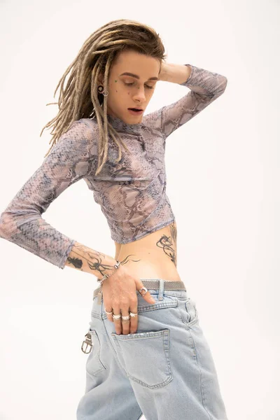 Trendy queer person in jeans and crop top with animal print posing isolated on white — стоковое фото