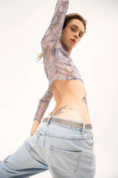 Low angle view of tattooed nonbinary person in crop top standing isolated on white - foto de stock