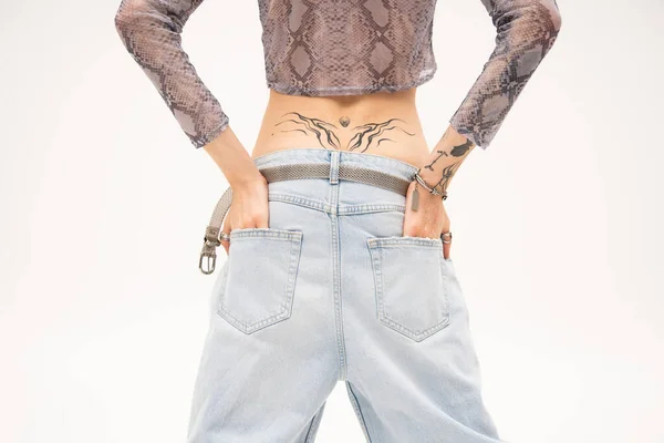 Vue recadrée d'une personne queer tatouée tenant la main dans des poches de jeans isolées sur du blanc — Photo de stock