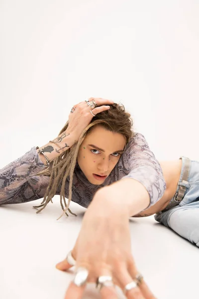 Tattooed nonbinary person looking at camera while lying on white background - foto de stock
