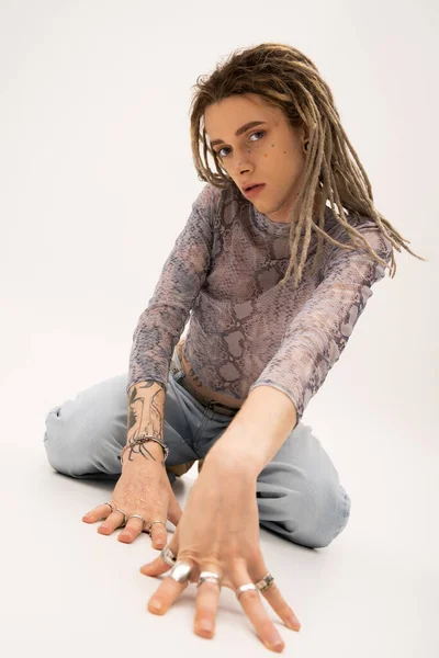 Tattooed queer person with rings on fingers looking at camera on white background - foto de stock