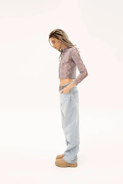 Side view of stylish queer person in crop top and jeans standing on white background — Stock Photo
