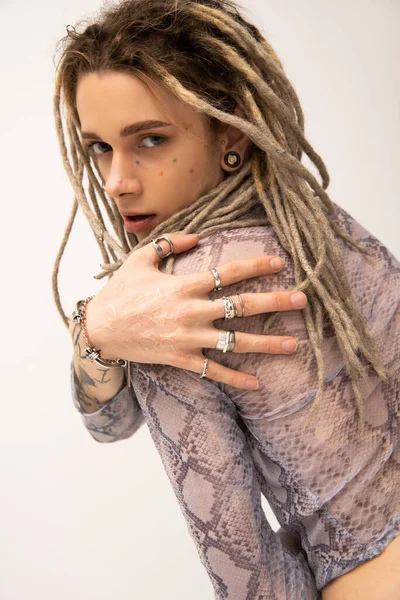 Young queer person with dreadlocks and silver finger rings looking at camera isolated on white — стоковое фото