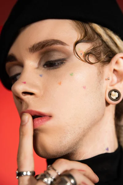 Close up portrait of tattooed queer person with makeup touching lips isolated on orange - foto de stock