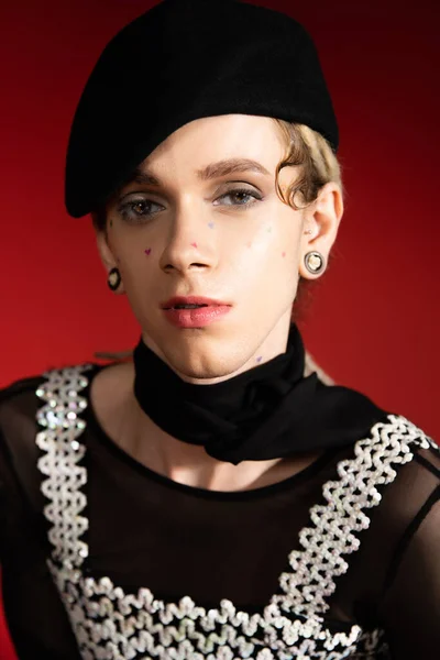 Portrait d'élégant modèle non binaire en béret noir et foulard regardant la caméra sur fond rouge — Photo de stock