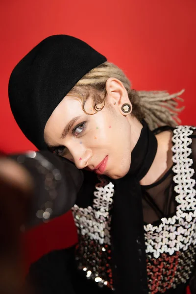 Portrait of queer model in elegant top and black beret looking at camera on red background — Stock Photo