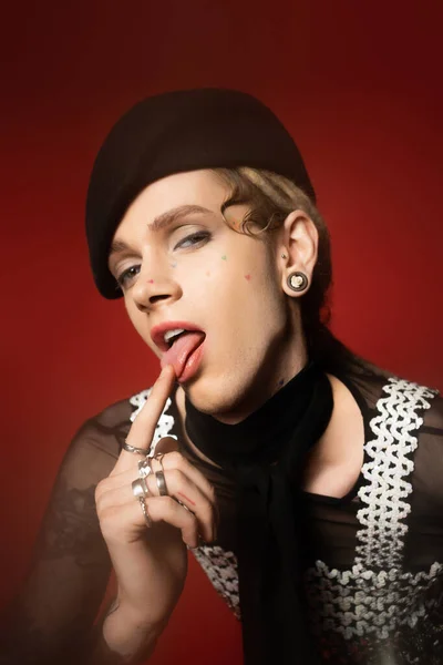 Queer person in elegant attire sticking out tongue and looking at camera on red background — Stockfoto