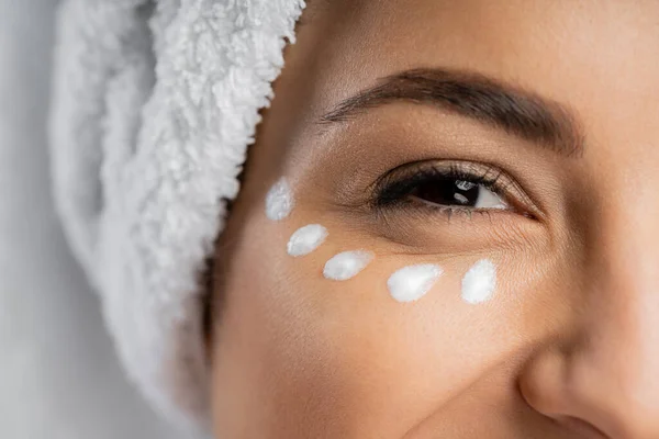 Cropped view of woman with towel and cream under eye isolated on grey — Stock Photo