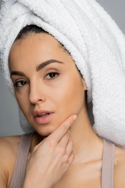 Portrait of young woman with towel on head touching face isolated on grey — Stockfoto
