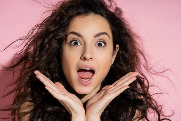 Portrait of shocked curly woman looking at camera on pink background — Fotografia de Stock