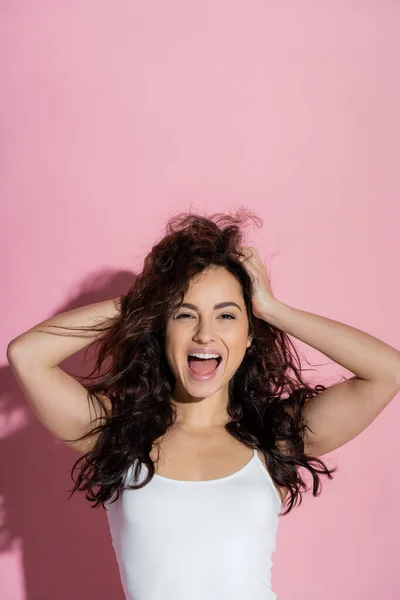 Excited curly woman touching hair on pink background — Stock Photo