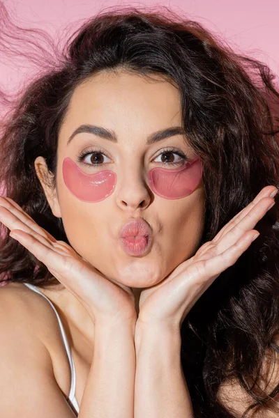 Portrait of curly woman with hydrogel eye patches pouting lips on pink background — Foto stock