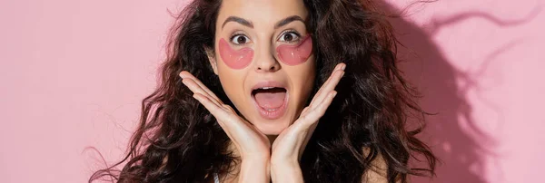 Excited brunette woman with hydrogel eye patches on face on pink background, banner — Stock Photo
