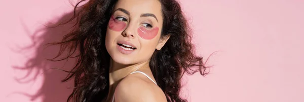 Positive young woman with hydrogel eye patches standing on pink background, banner — Stock Photo