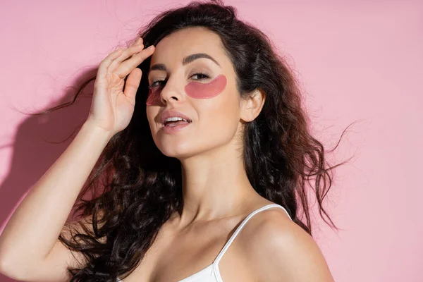 Pretty woman with hydrogel eye patches touching forehead on pink background — Stock Photo