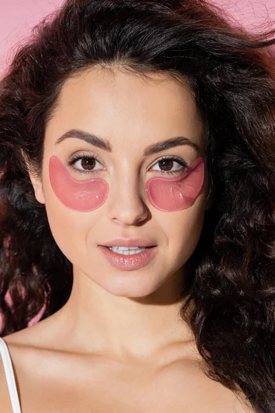 Portrait of curly young woman with hydrogel eye patches on pink background — Stock Photo