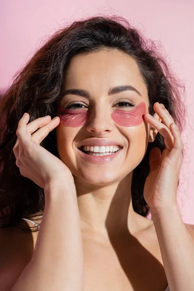 Portrait of curly young woman with hydrogel eye patches on pink background — Stockfoto
