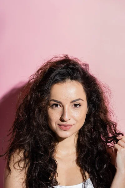 Portrait of curly woman with freckles looking at camera on pink background — Foto stock