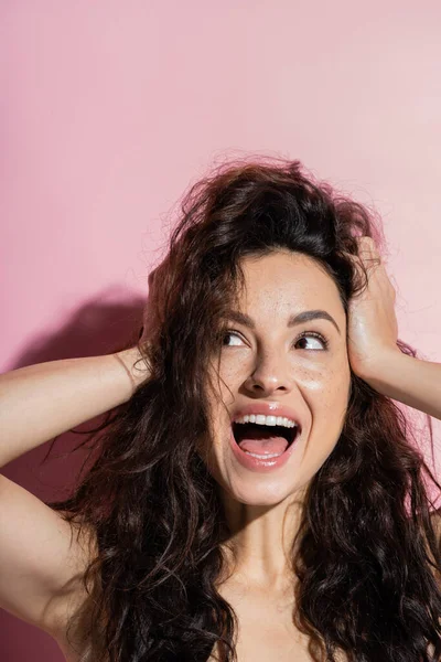 Excited brunette woman with freckled looking away on pink background - foto de stock
