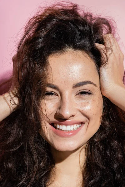 Portrait of positive woman with freckles touching hair on pink background — Stock Photo