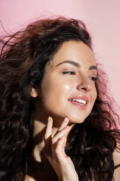 Positive young woman with freckles touching face isolated on pink — Stock Photo