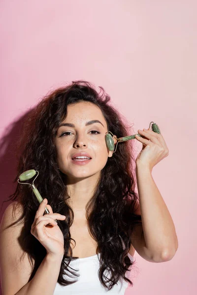 Pretty freckled woman using jade roller on face on pink background — Stock Photo