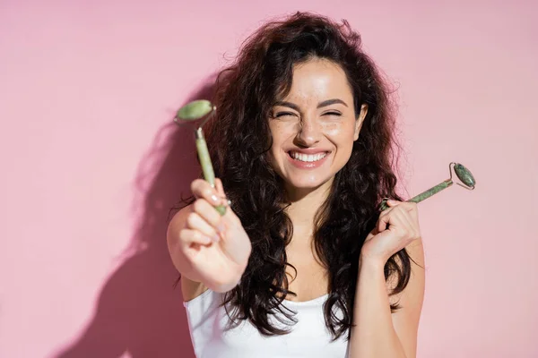 Positive freckled woman holding jade rollers on pink background — Stock Photo