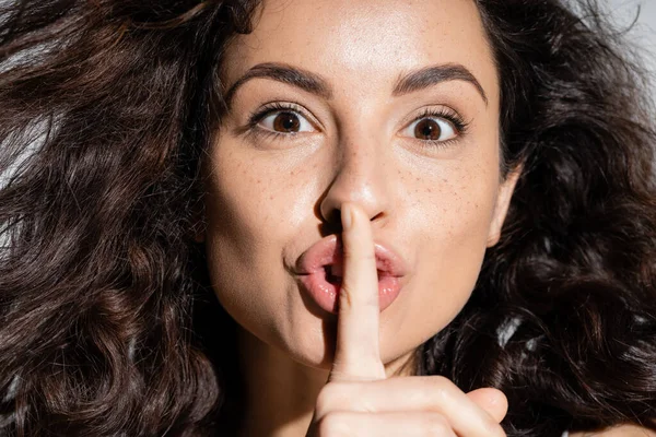 Portrait of curly freckled woman showing secret gesture isolated on grey — Stockfoto