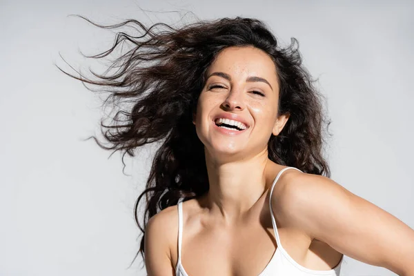 Happy young woman with curly hair looking at camera isolated on grey — Stock Photo