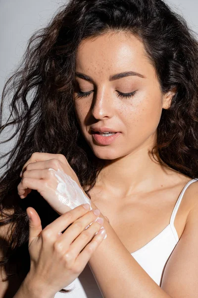 Pretty brunette woman applying cream on hand isolated on grey — Stockfoto