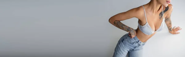 Vista ritagliata di seducente donna in jeans e reggiseno in posa con mano sul fianco vicino cubo su sfondo grigio, banner — Foto stock