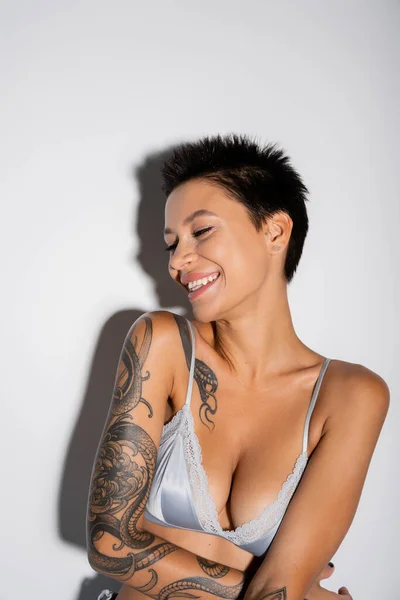 Портрет татуйованої жінки в блакитному атласі, посміхаючись на сірому фоні — стокове фото