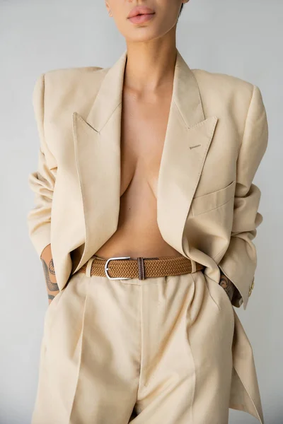 Vista recortada de la mujer sexy con chaqueta en el cuerpo sin camisa y cogidas de la mano en bolsillos de pantalones aislados en gris - foto de stock