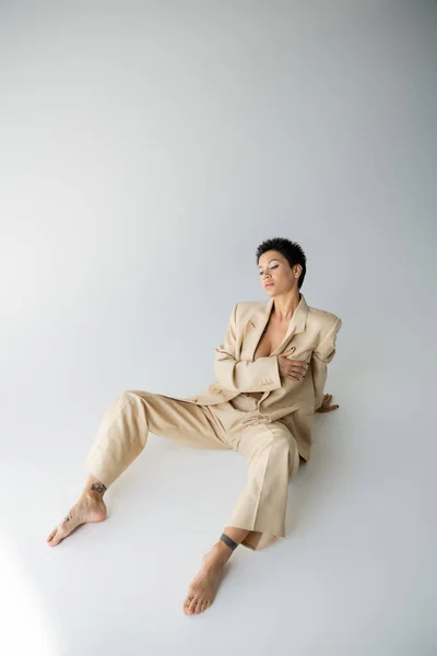 High angle view of sexy shirtless woman in beige suit sitting on grey background — Stock Photo