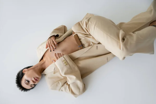 Top view of shirtless woman in trendy pantsuit covering breast with hands while lying on grey background — Stock Photo