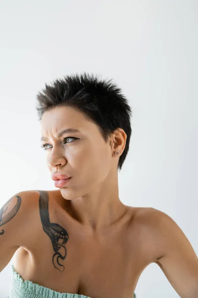 Портрет незадоволеної татуйованої жінки в розтяжці зверху дивиться ізольовано на сірому — стокове фото