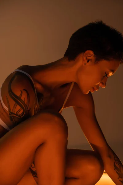 Sexy tattooed woman with short brunette hair posing in light on dark background — Fotografia de Stock