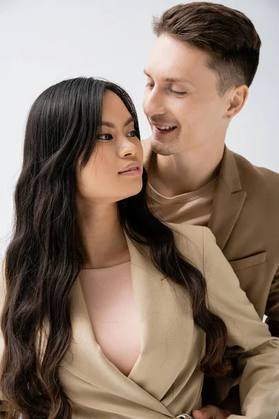 Homem feliz olhando elegante asiático mulher com longo morena cabelo isolado no cinza — Fotografia de Stock