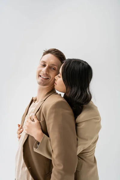 Morena asiático mulher abraçando alegre homem vestindo bege blazer isolado no cinza — Fotografia de Stock