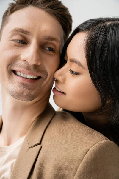 Young asian woman smiling near happy man in beige blazer isolated on grey — Stock Photo