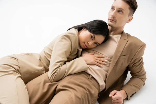 Sensual asian woman looking at camera while hugging trendy man lying on white background — Stock Photo