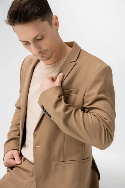 Brunette man touching beige stylish blazer while posing on white background — Stock Photo