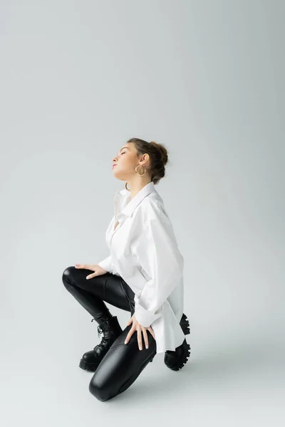 Full length of stylish woman in white oversize shirt and black tight pants posing on grey background — Stockfoto