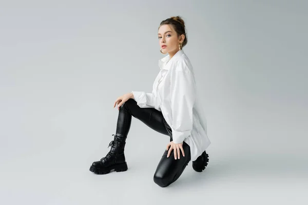 Trendmodel in schwarzer Latex-Hose und Oversize-Shirt mit Blick in die Kamera auf grauem Hintergrund — Stockfoto