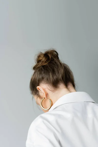 Vista trasera de mujer joven en pendiente de aro dorado y camisa blanca aislada en gris — Stock Photo