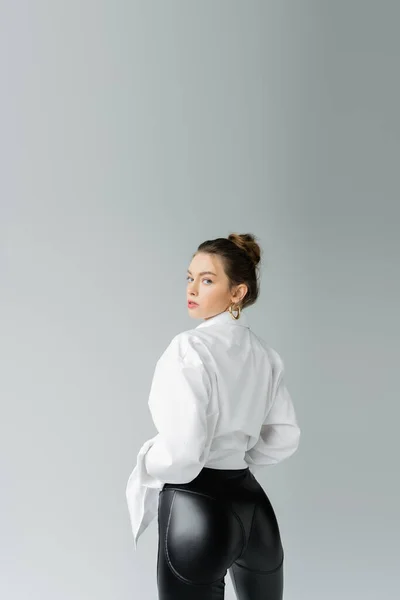 Sexy woman in white shirt and black tight pants looking at camera isolated on grey — Stock Photo