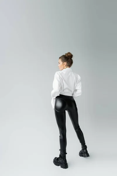 Back view of sexy woman in black latex pants and rough boots standing on grey background — Stockfoto